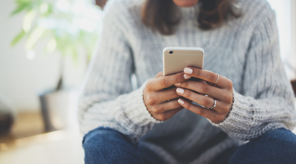 Cropped image of black female in gray turtle neck sweater texting on her phone