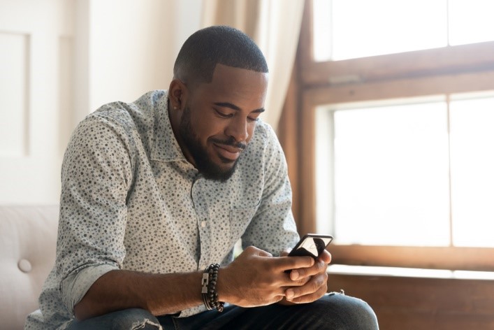 African American male sitting smiling while texting on his phone