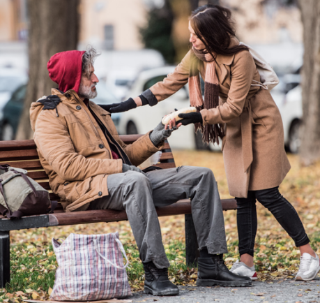 A woman offering a hand approaching a homeless man sitting on a bench