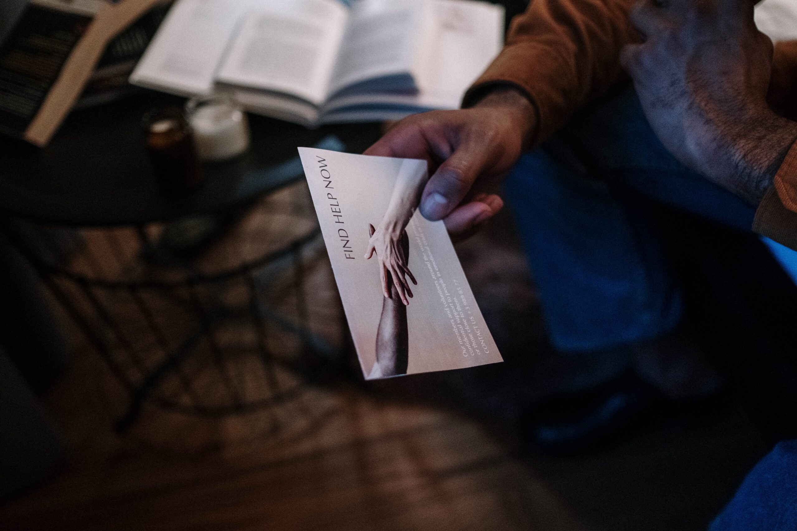 The hand of an African American male holding a postcard depicting white and black arms stretching toward each other and says "Find Help Now"